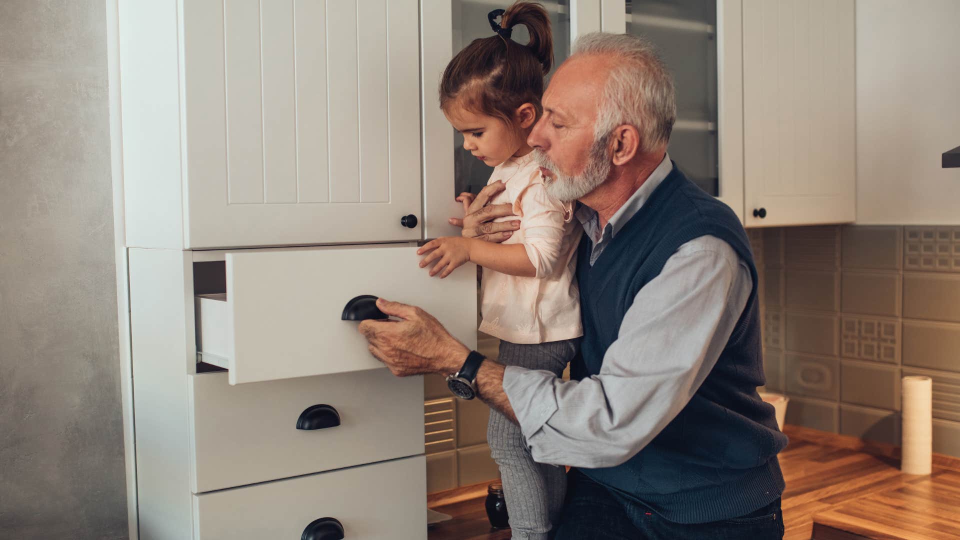 Man opening junk drawers with his granddaughter in the kitchen.