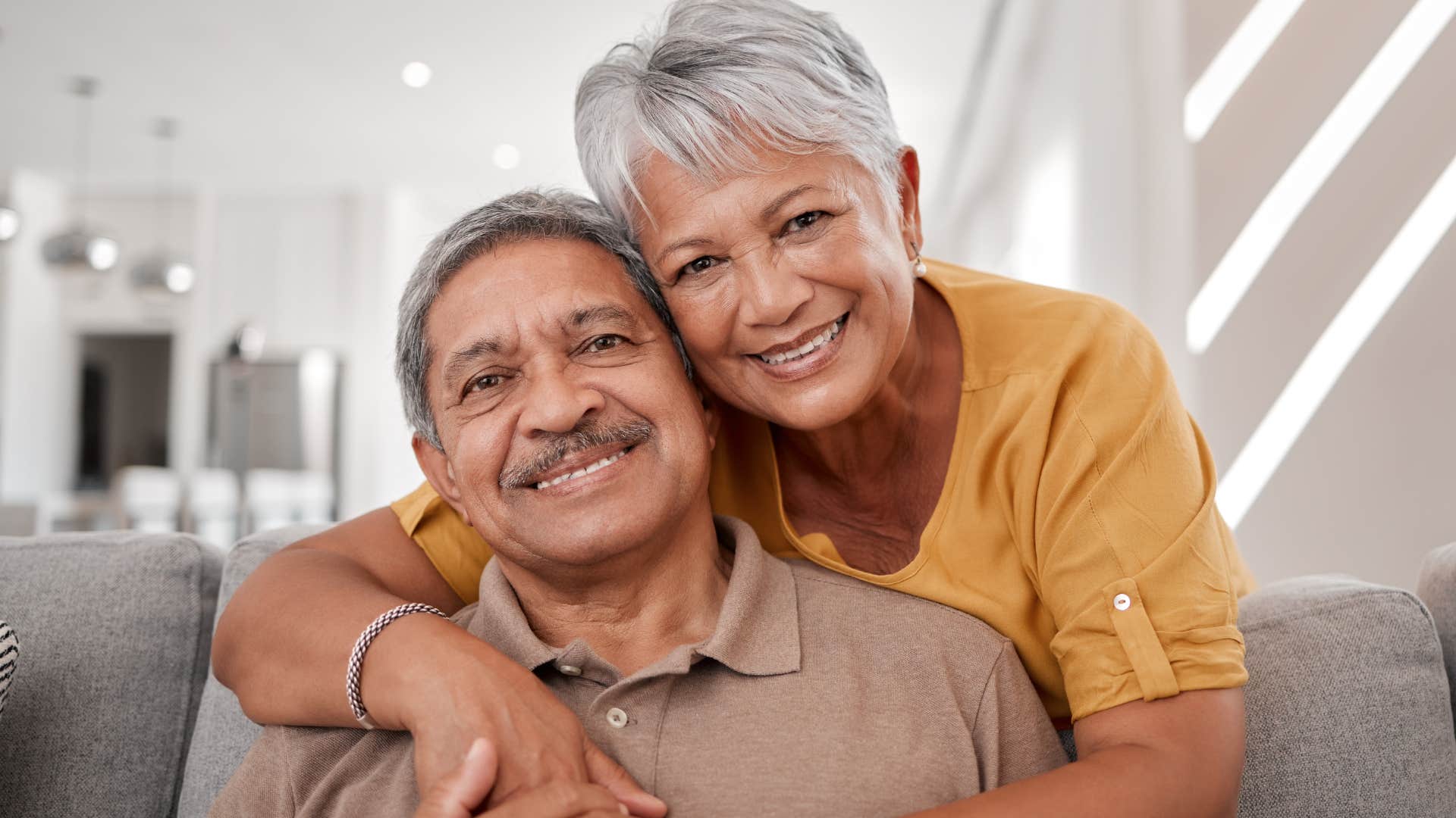 Older couple smiling and sitting in their house with Beige walls and neutral colors.