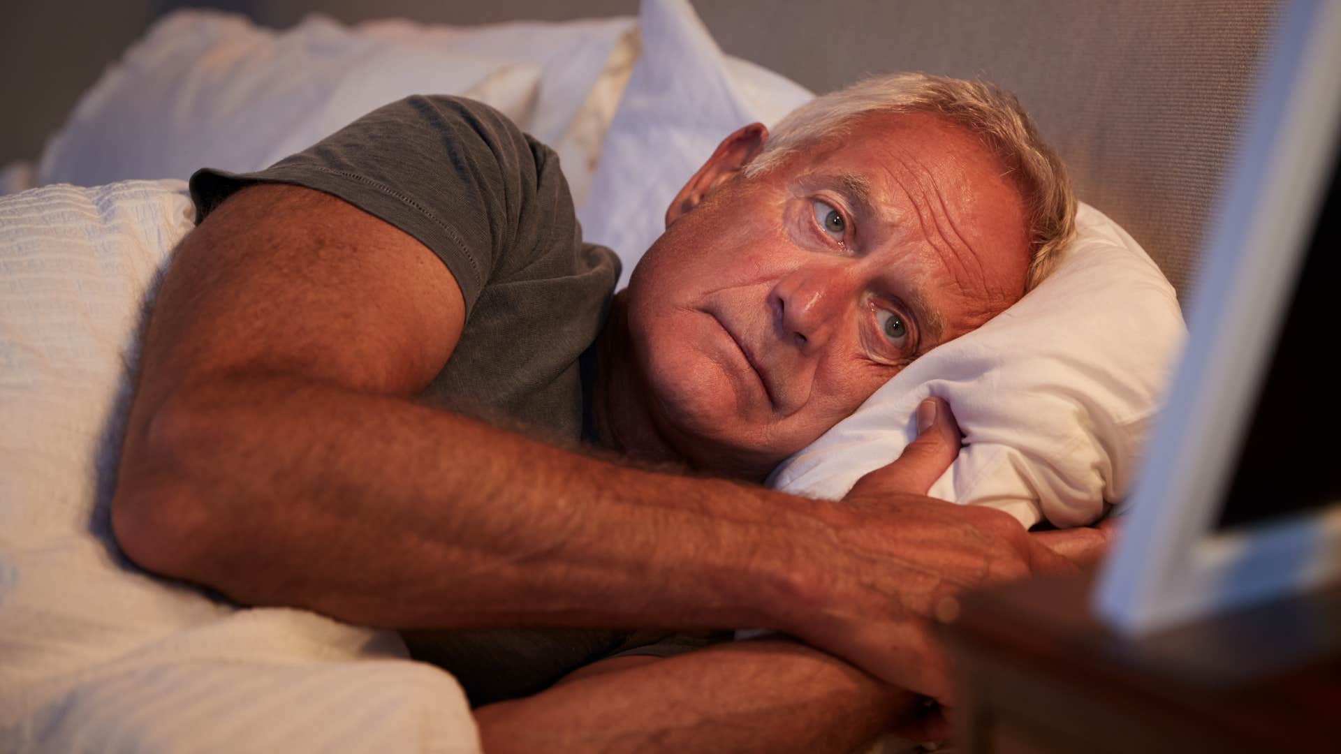 man laying awake on an uncomfortable mattress