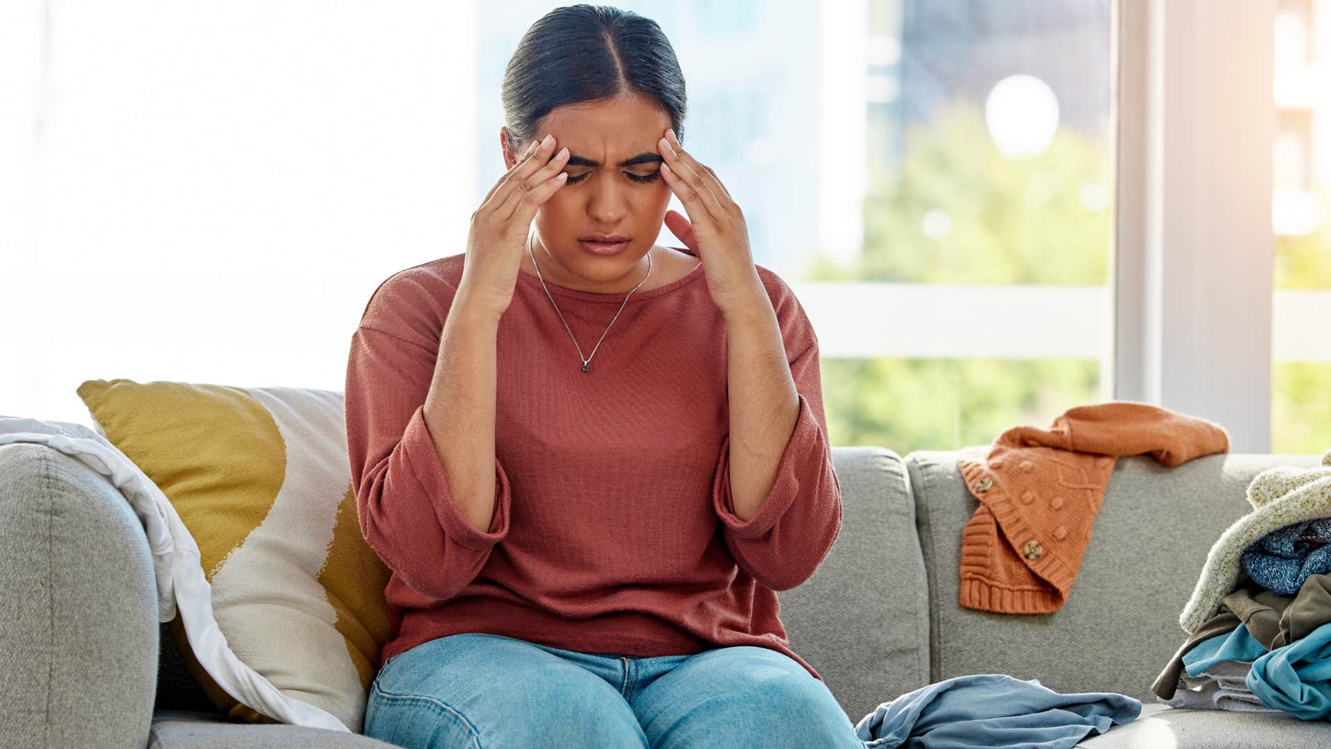 Woman holding her head at home surrounded by clutter.