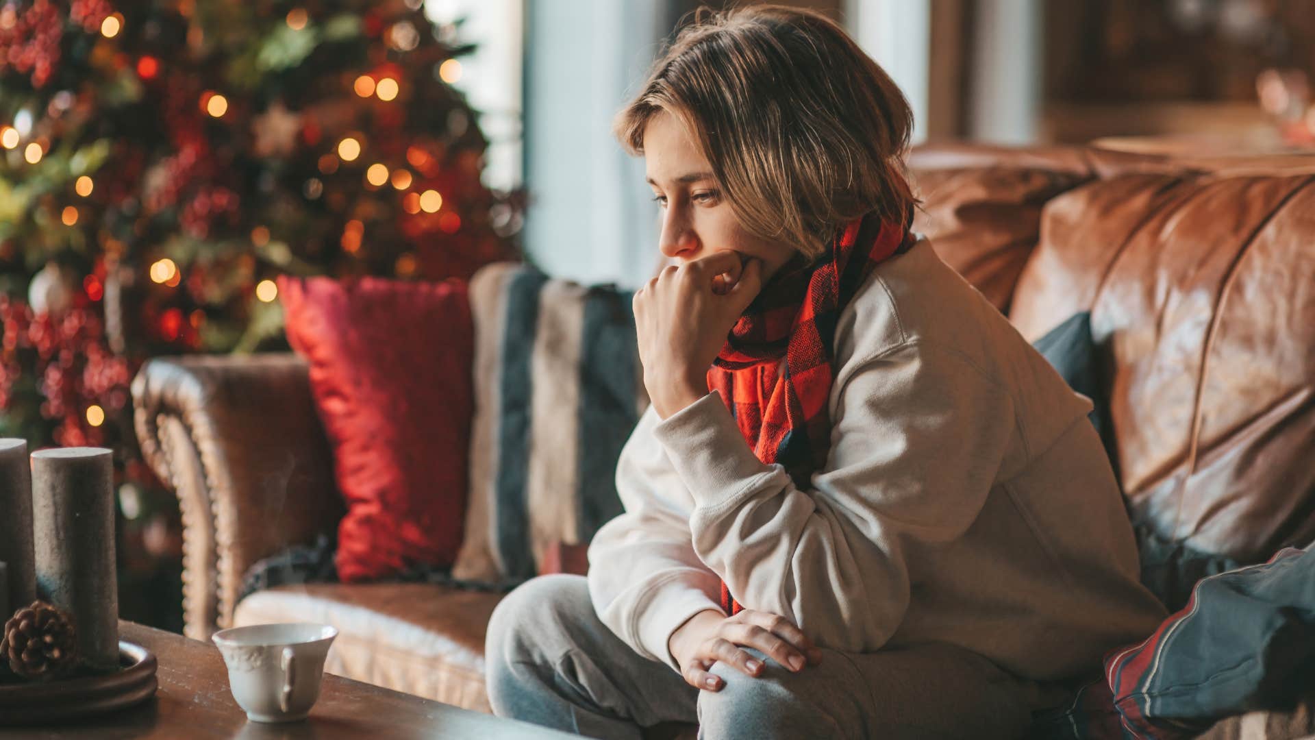 Sad woman sitting on a couch surrounded by lingering holiday decorations.