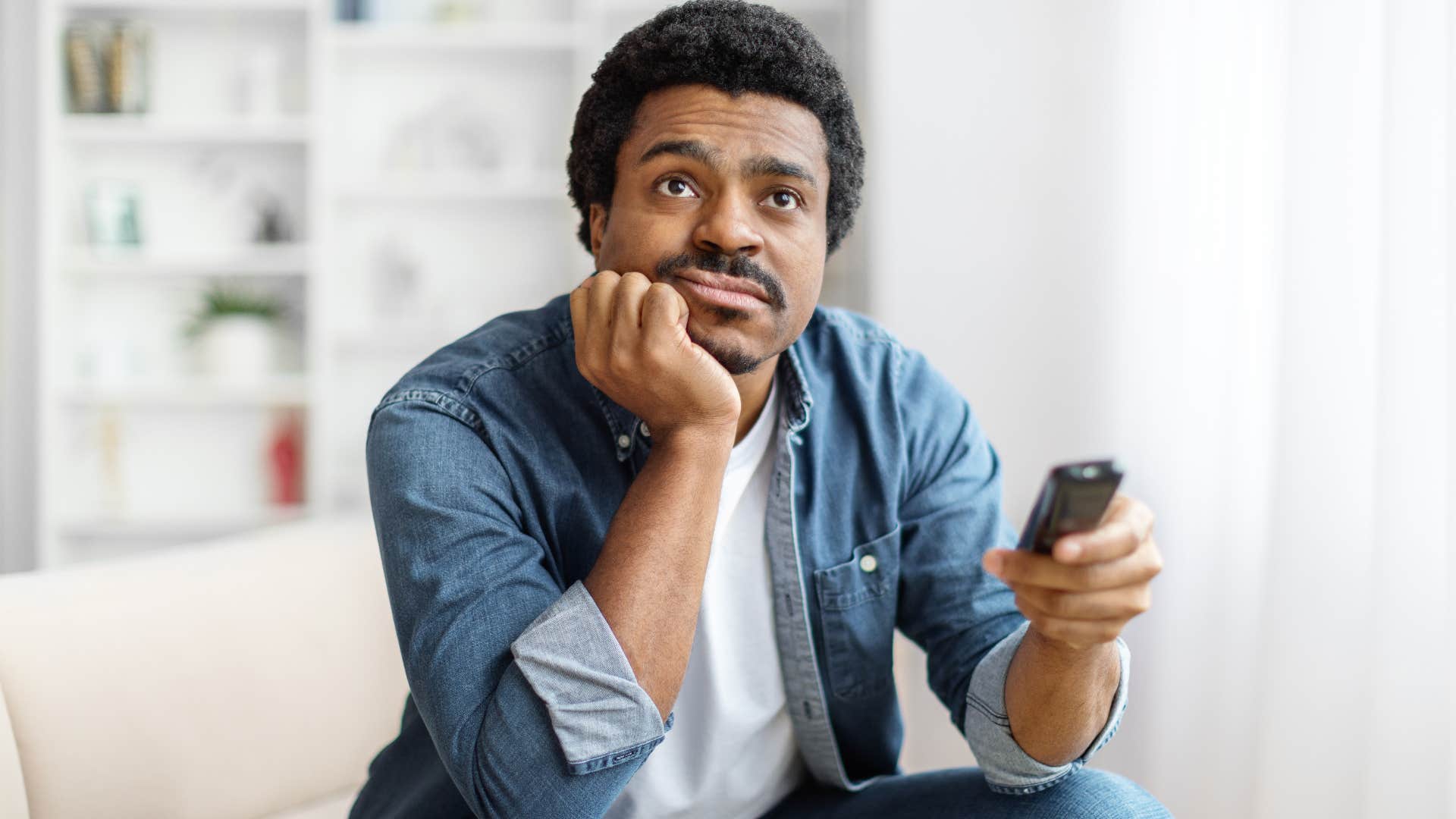 Man watching TV in his house with no books.