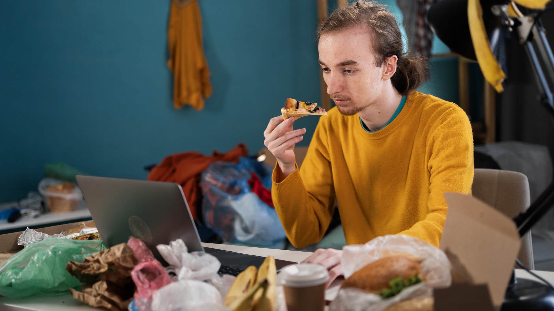 Man eating food surrounded by empty takeout containers at home.