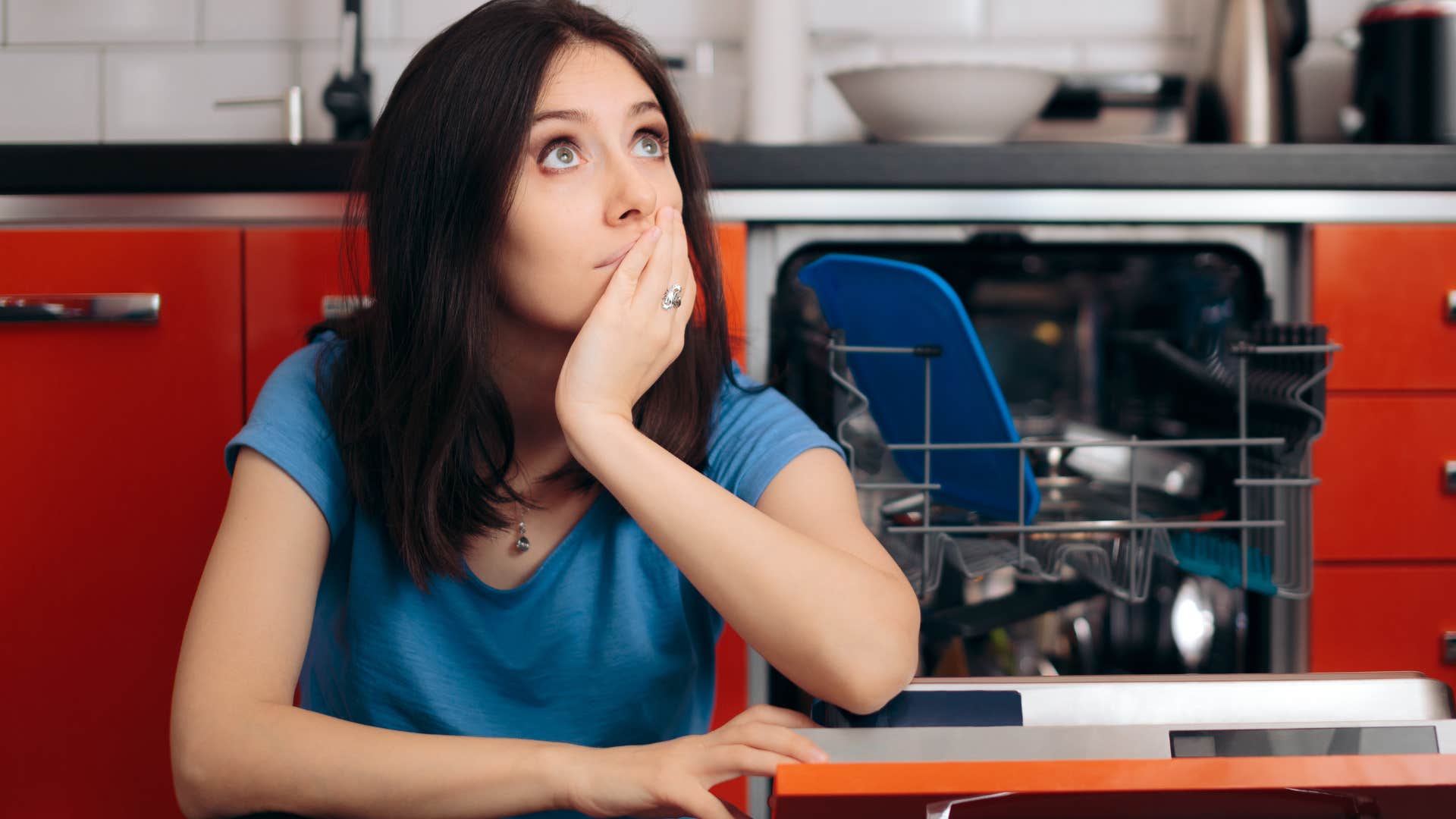 woman sitting next to broken appliance dishwasher at home