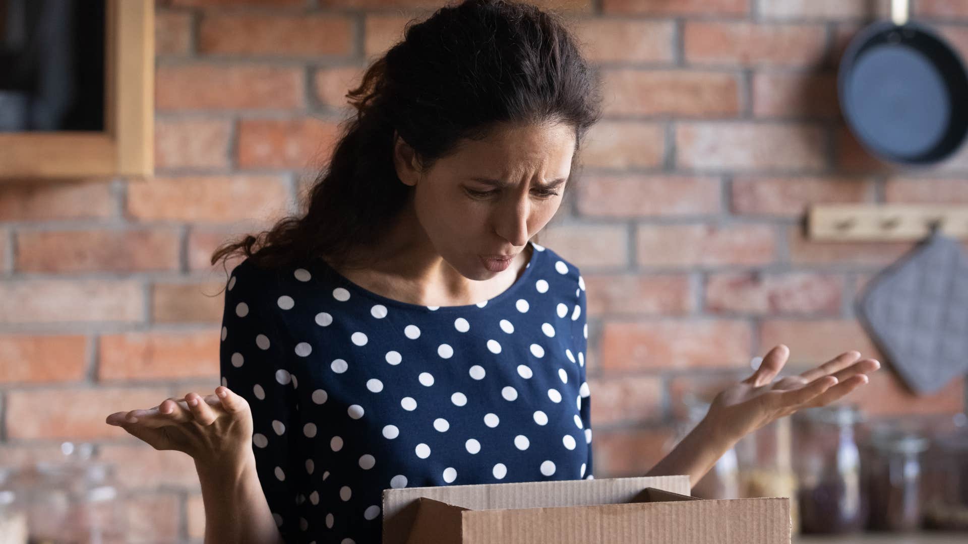 upset woman looking in a box of mismatched tupperware in her kitchen