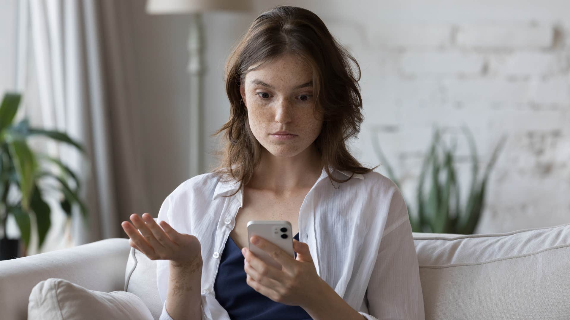 woman in white shirt staring at phone in shock and annoyance as person calls instead of texts