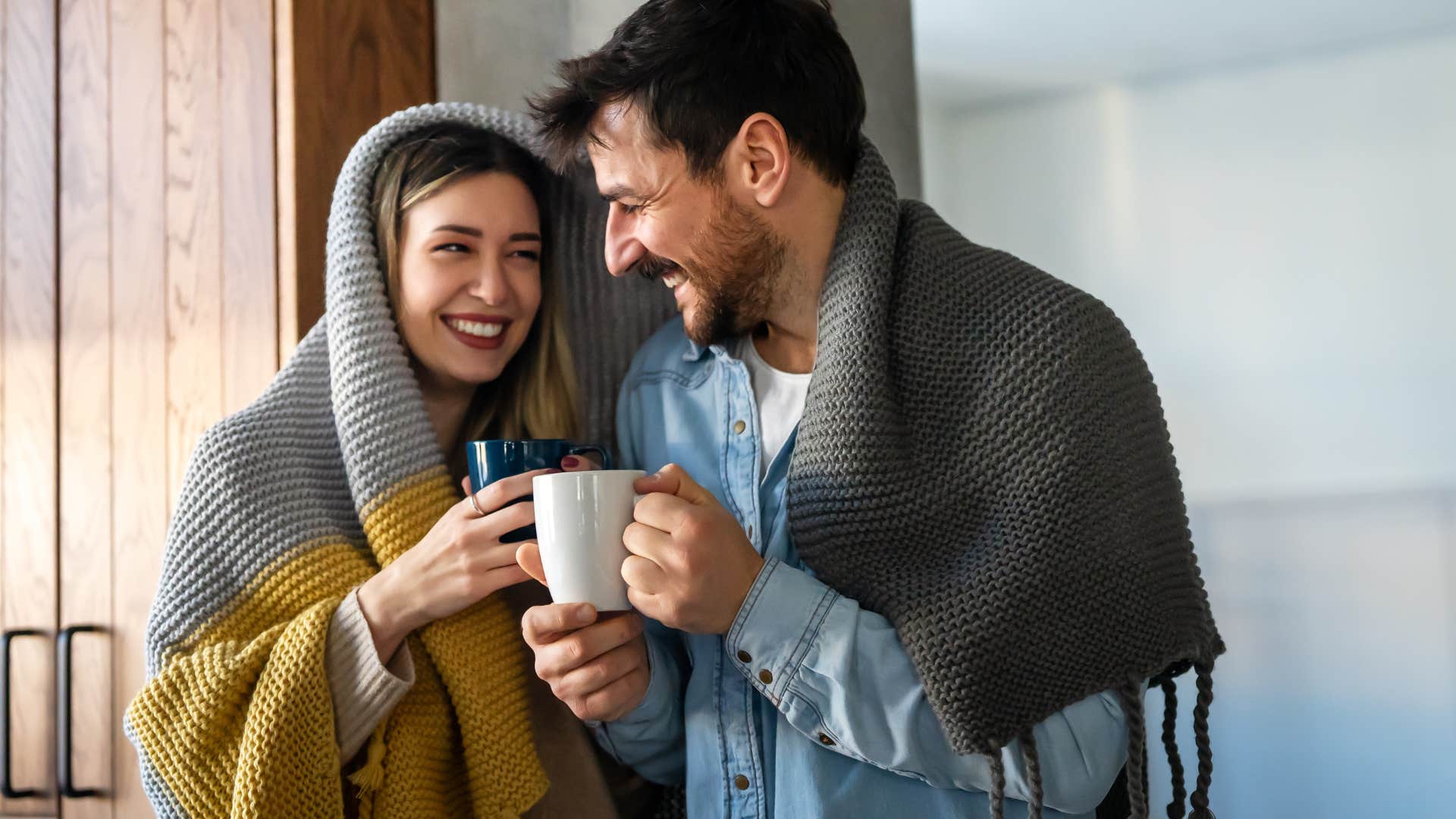 couple drinking hot coffee snuggled underneath blankets