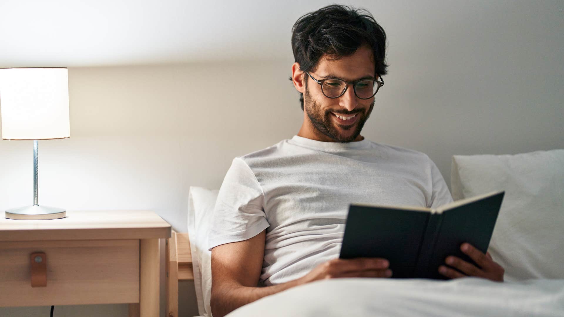 Man reading next to his coordinating nightstands in bed.
