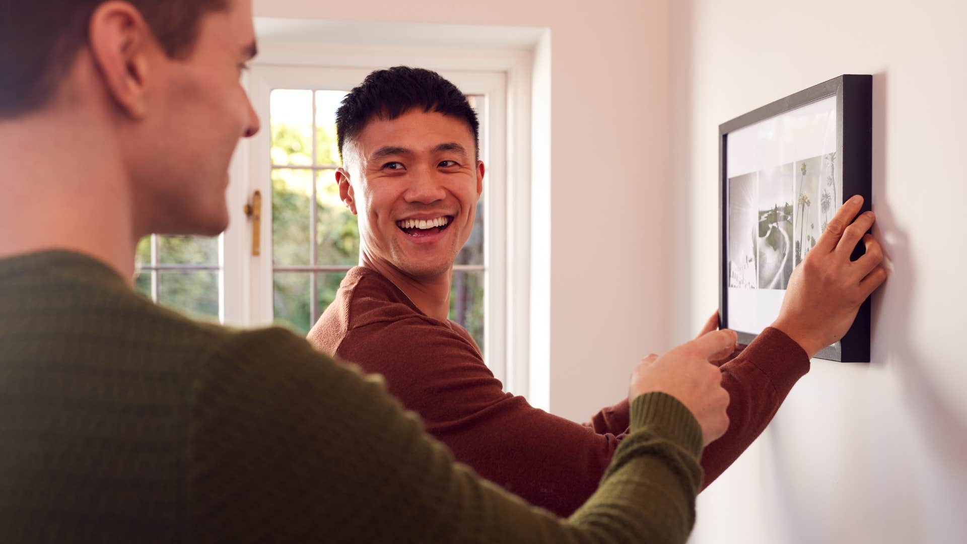 Man putting up a couple's photo wall with his partner at home.