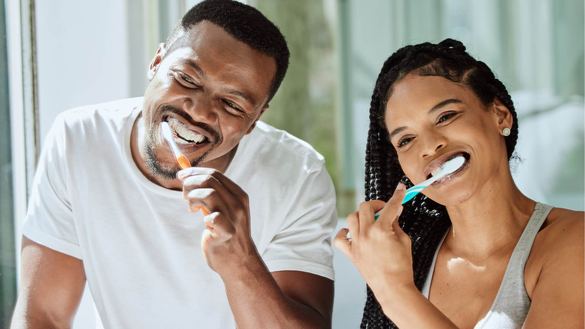 Couple smiling in the bathroom with more than one toothbrush.