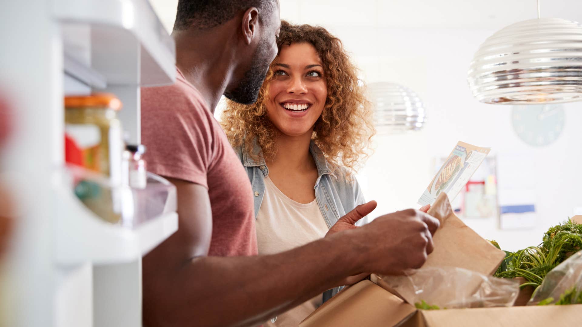 Couple unpacking two kinds of groceries into their fridge.