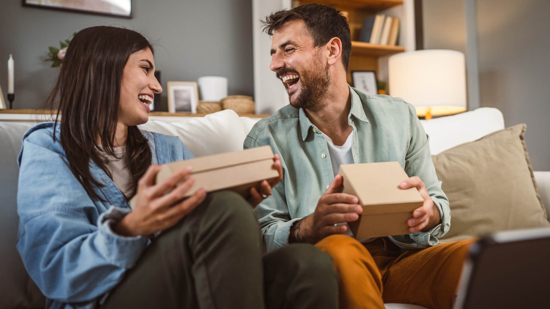 Couple smiling and opening random wedding gifts at home.