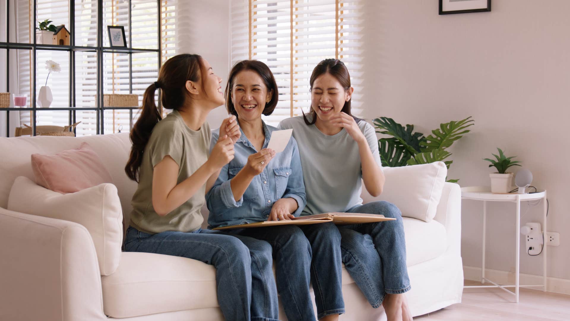 three friends looking through photo album on the couch