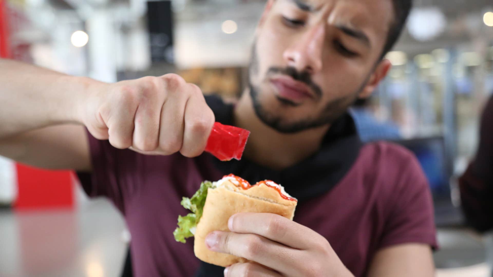 man using ketchup condiment on his sandwich