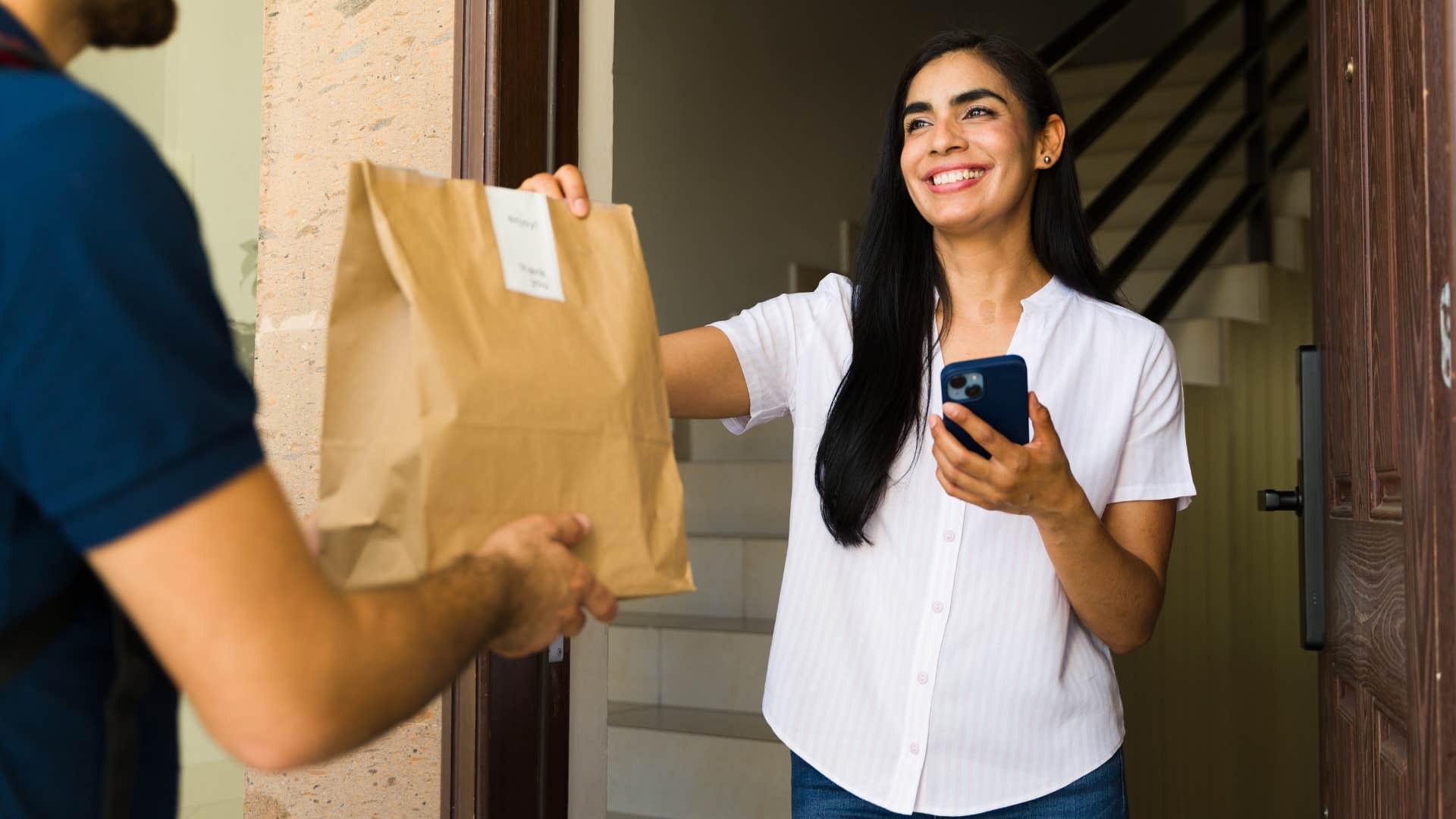 Woman smiling at her front door after ordering delivery.