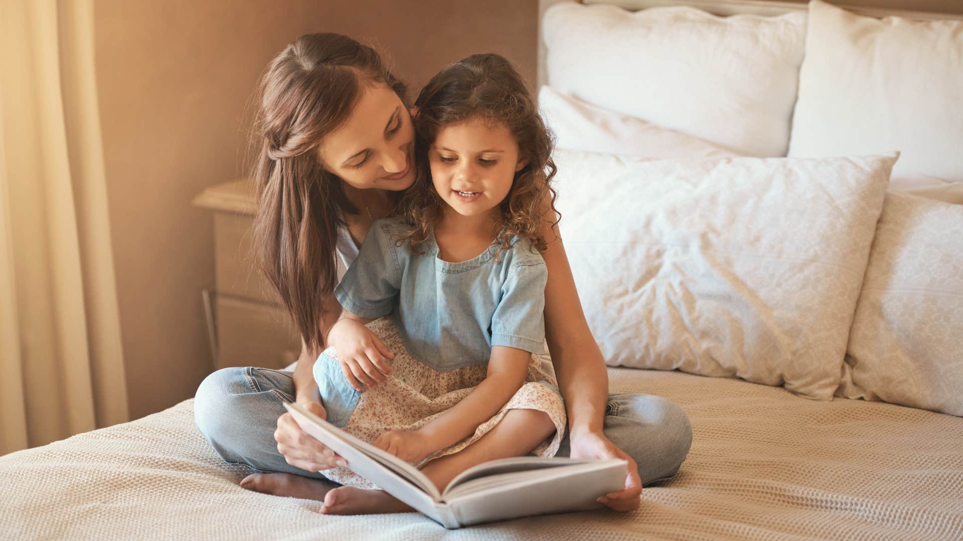 mom and daughter reading book on bed