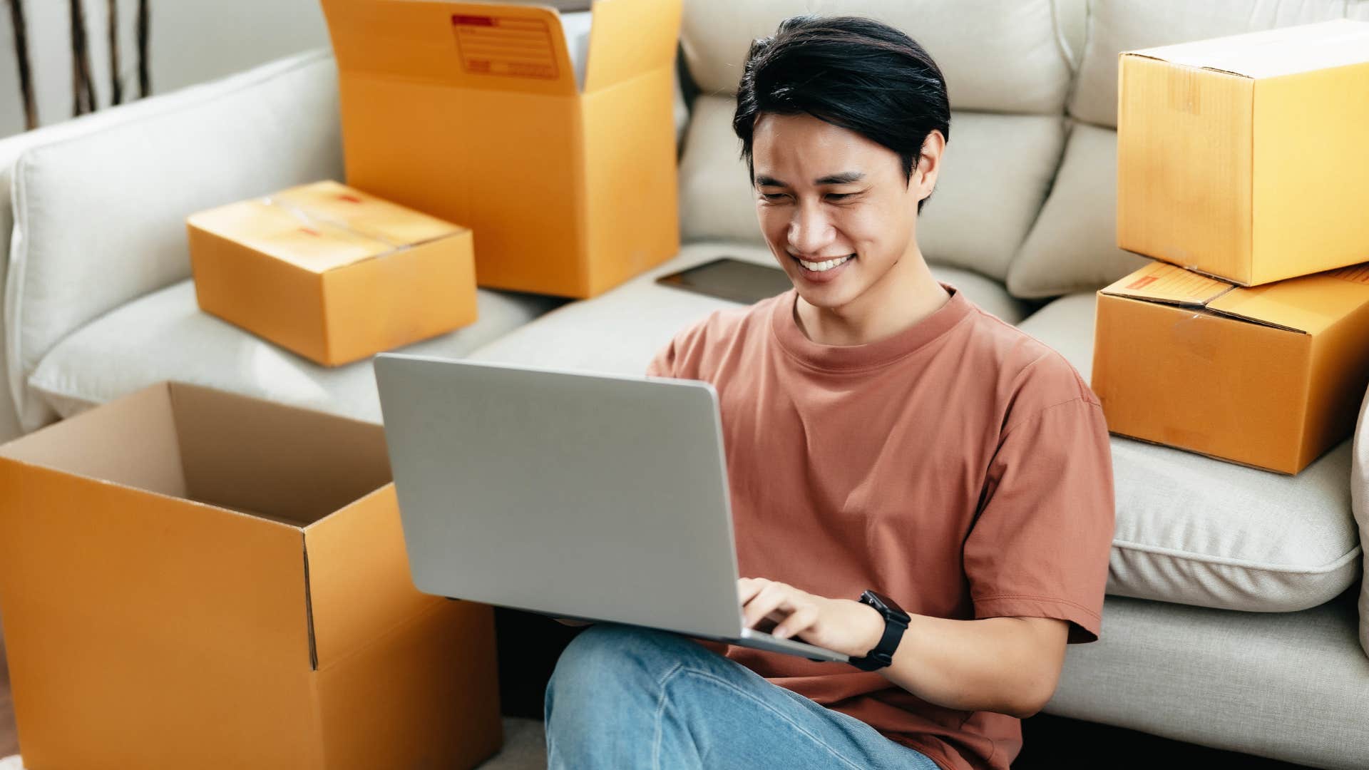 Man smiling in his living room surrounded by cardboard boxes.