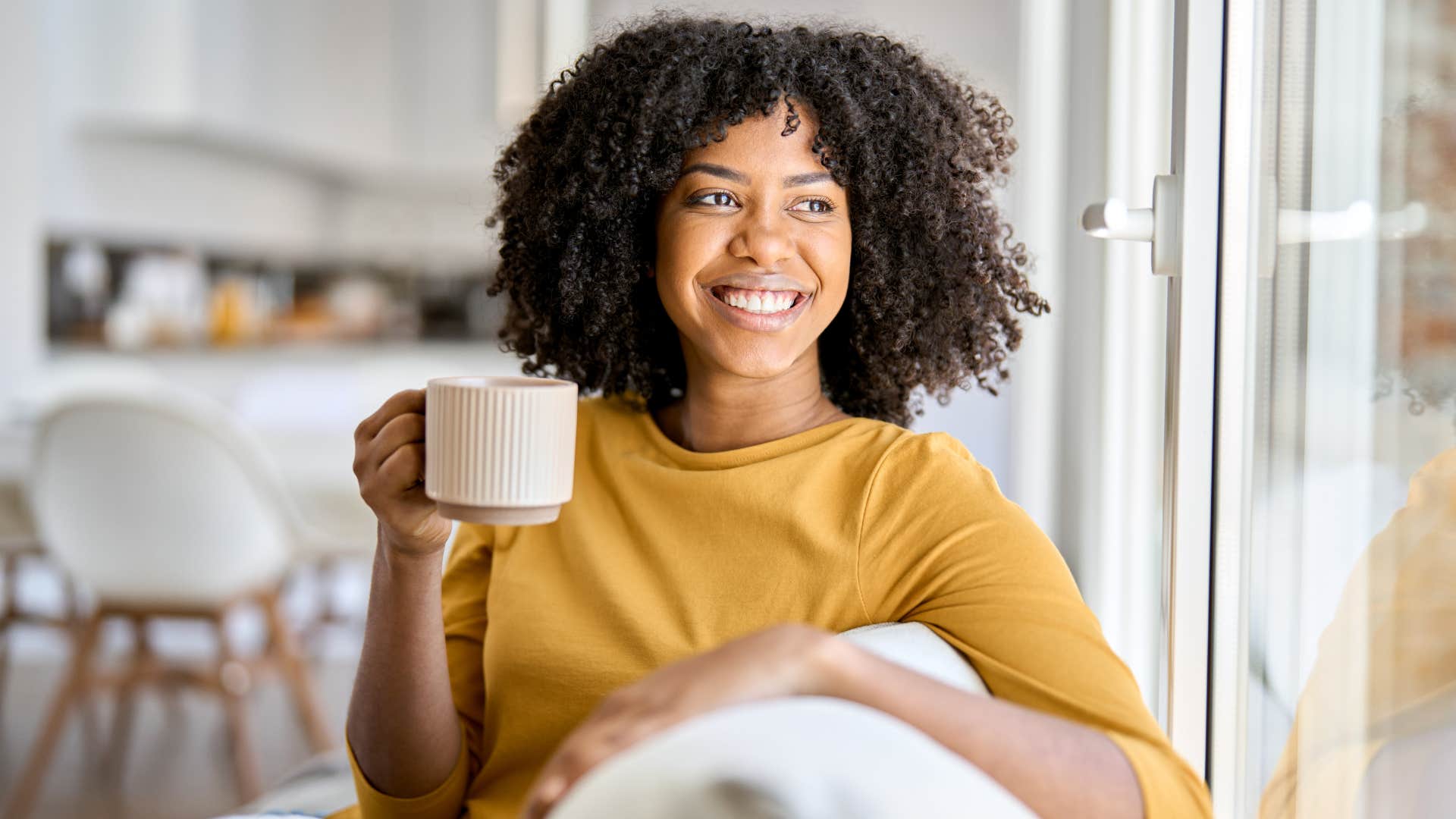 Woman smiling at home holding coffee mugs.