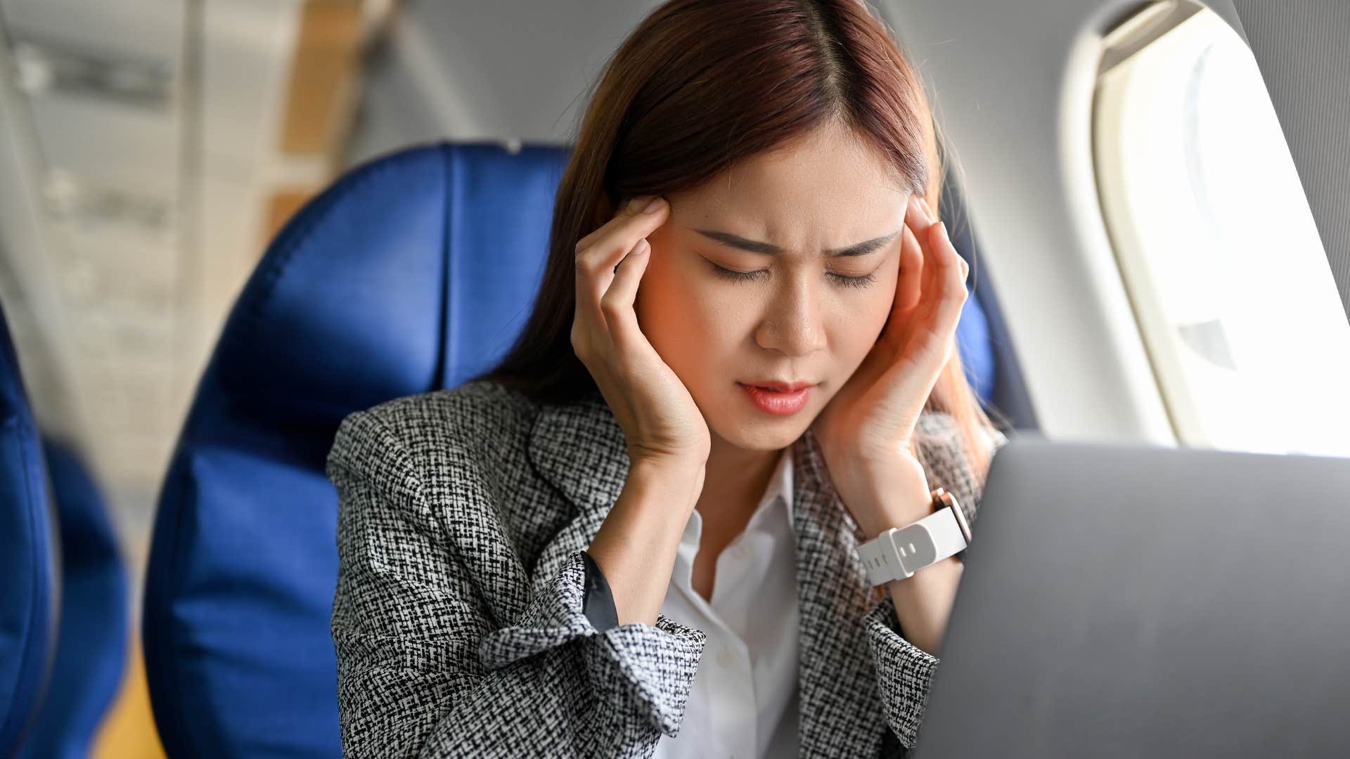 stressed woman flying coach working on a laptop