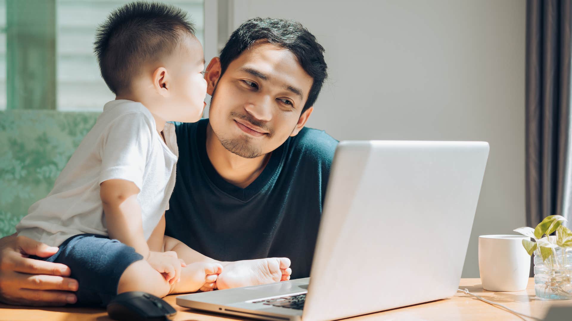Man who's being a stay-at-home parent working on his laptop next to a baby.