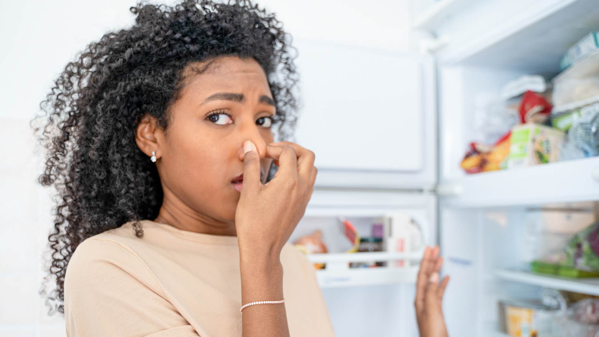 a woman smells something bad in her friends fridge