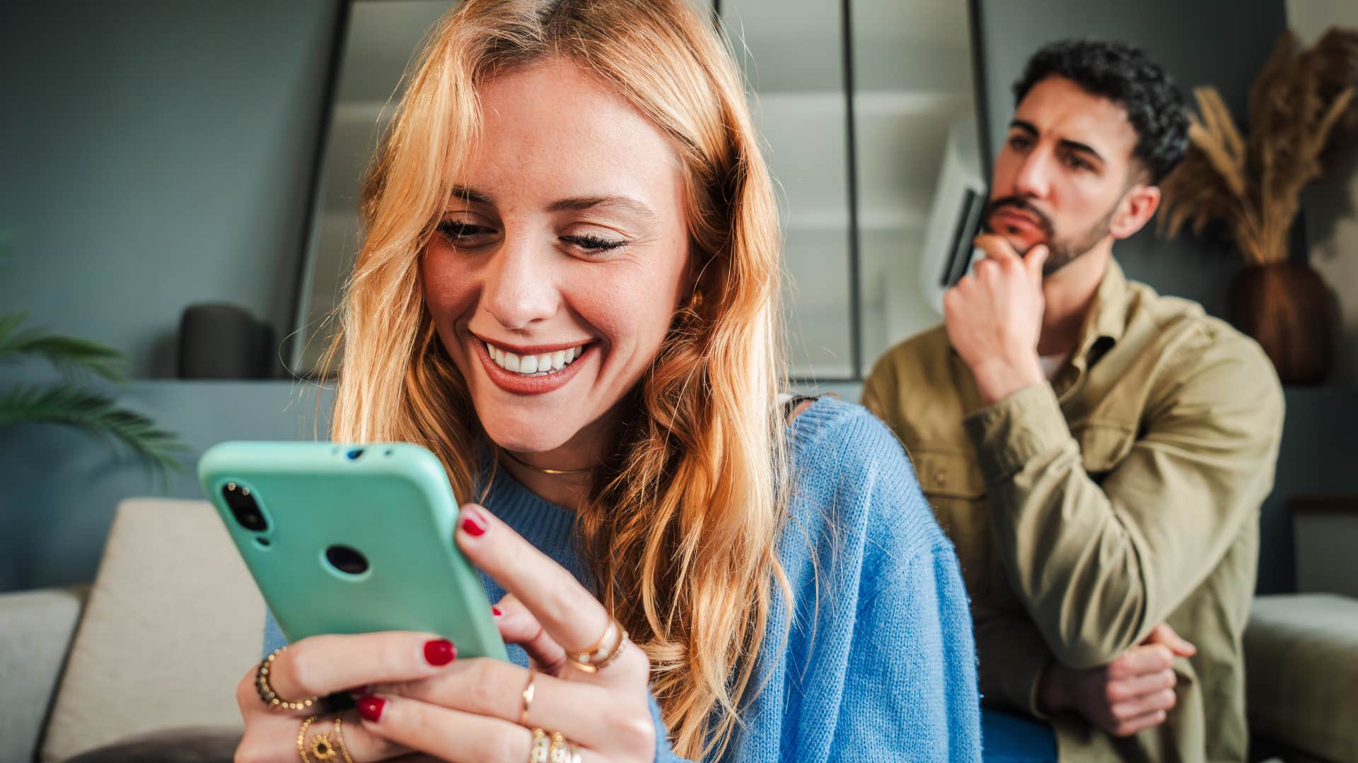 upset man sitting behind woman with little self-awareness on her phone
