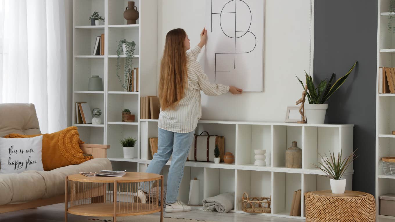 woman hanging up art at home