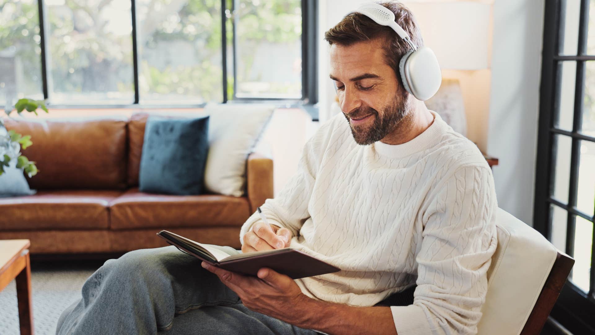 man smiling and writing in a journal at home