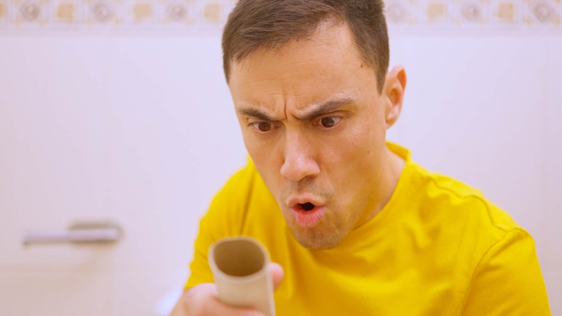 annoyed man holding empty toilet paper roll