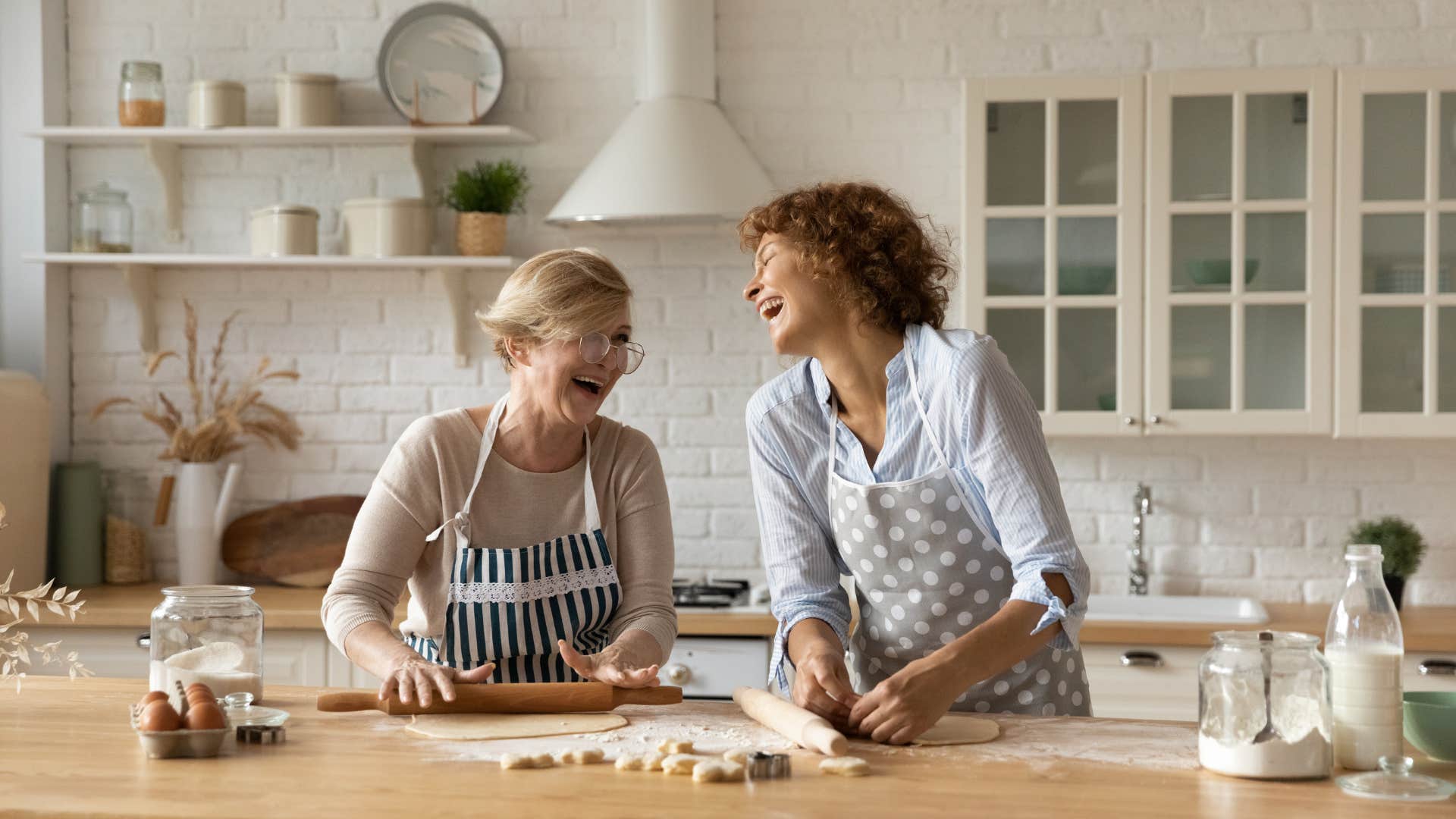 two upper middle class women laughing and cooking in kitchen with high end appliances