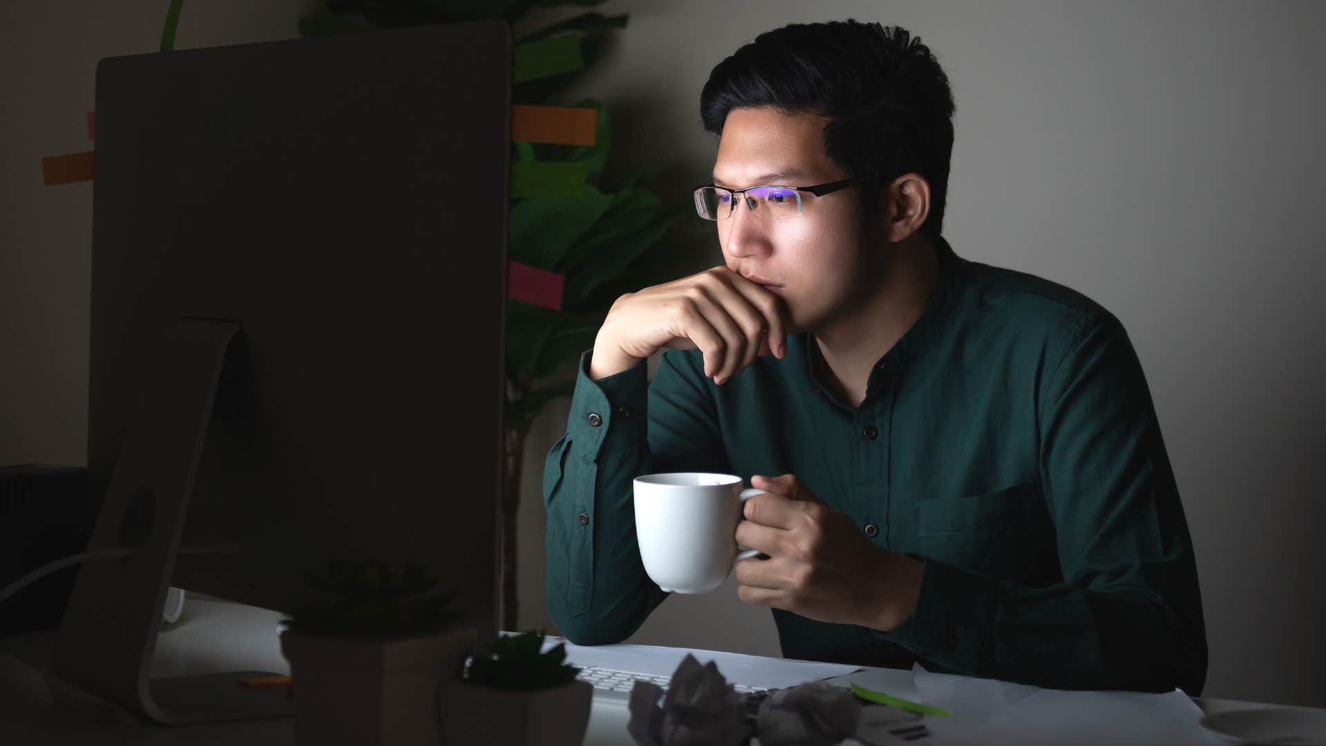 Man with empty coffee cups around him sitting in a dark room.