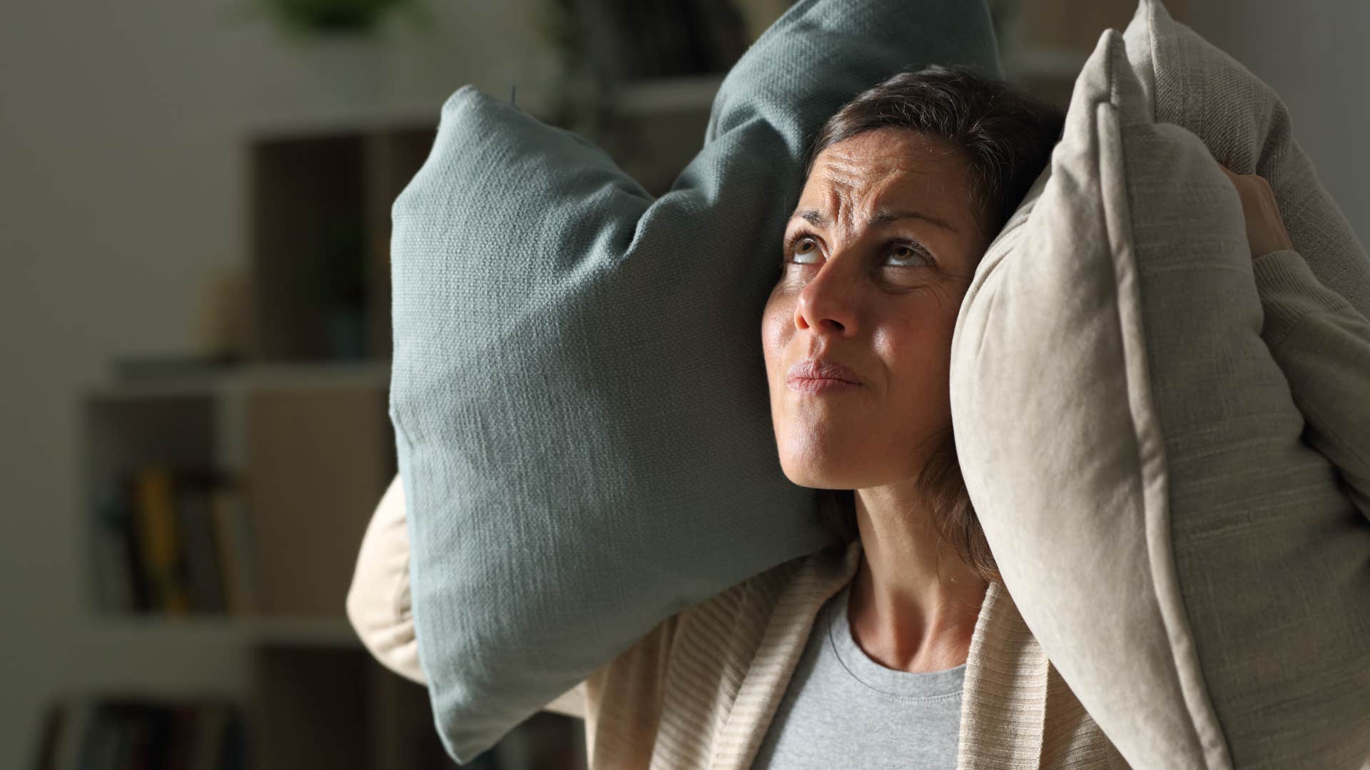 Woman covering her ears with pillows to block out unnecessary noise.