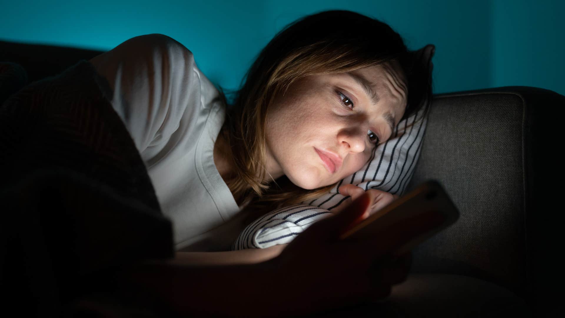 Woman with too many screens scrolling on her phone in the dark.