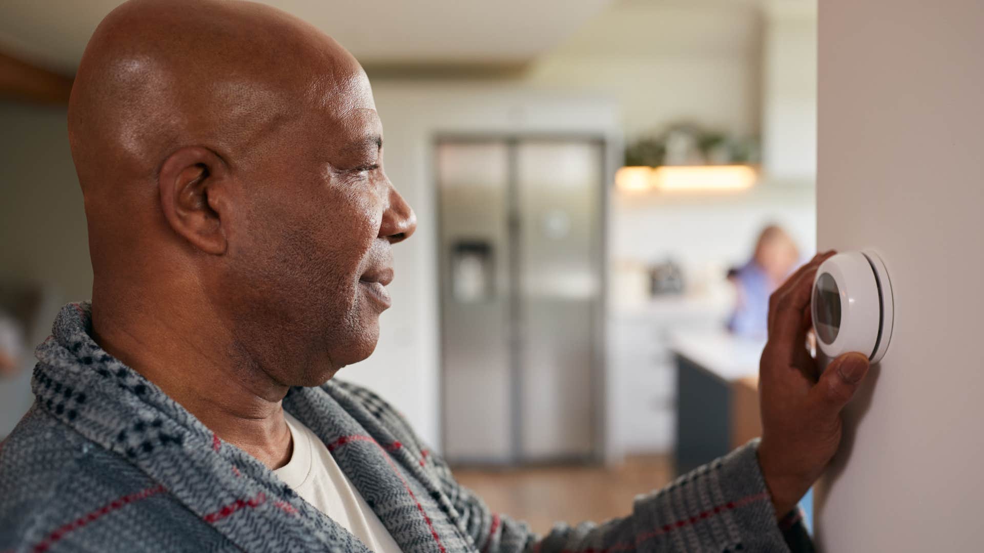 Man changing the thermostat in his warm bedroom.