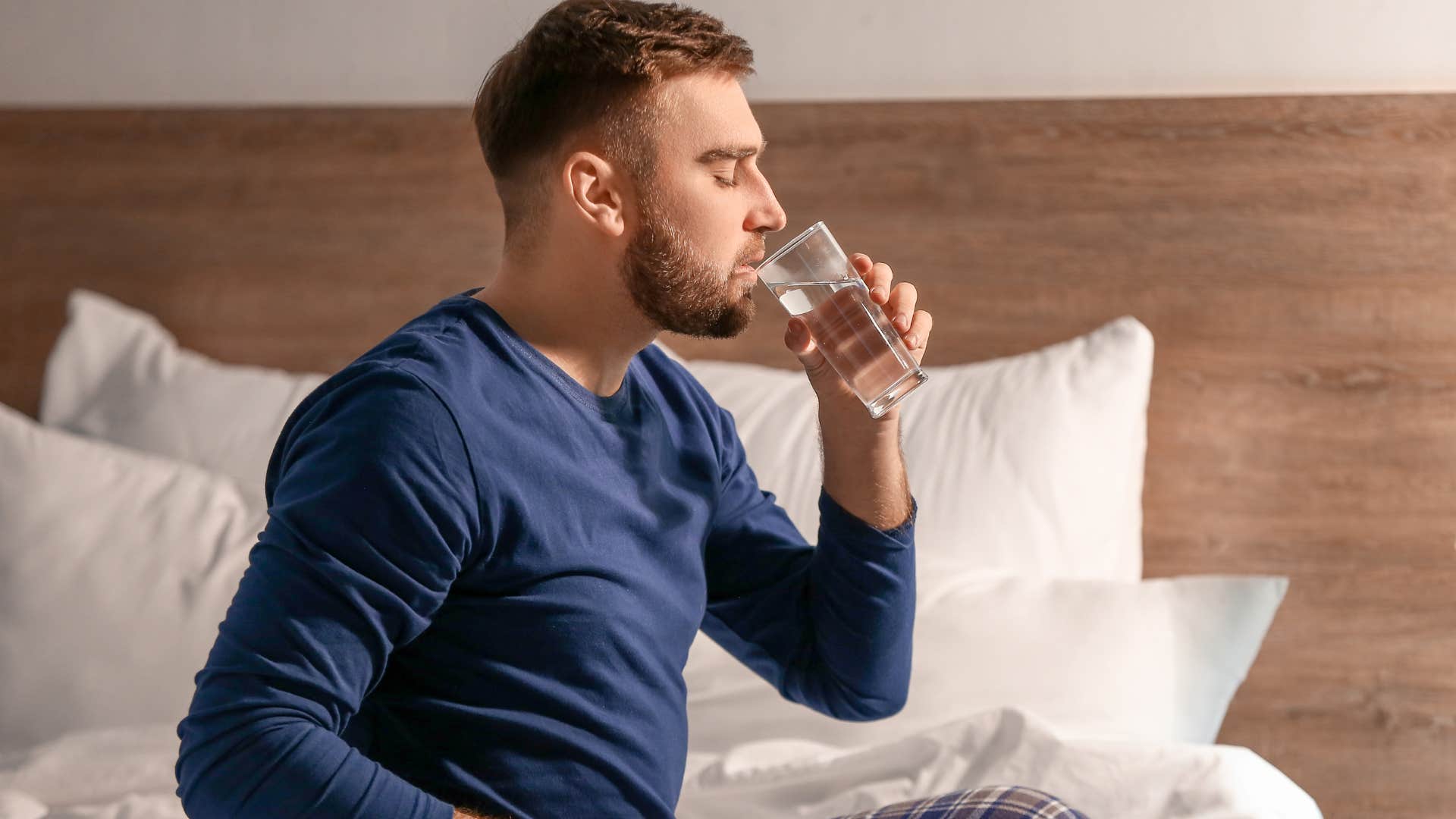 Man drinking water with water bottles next to their bed.