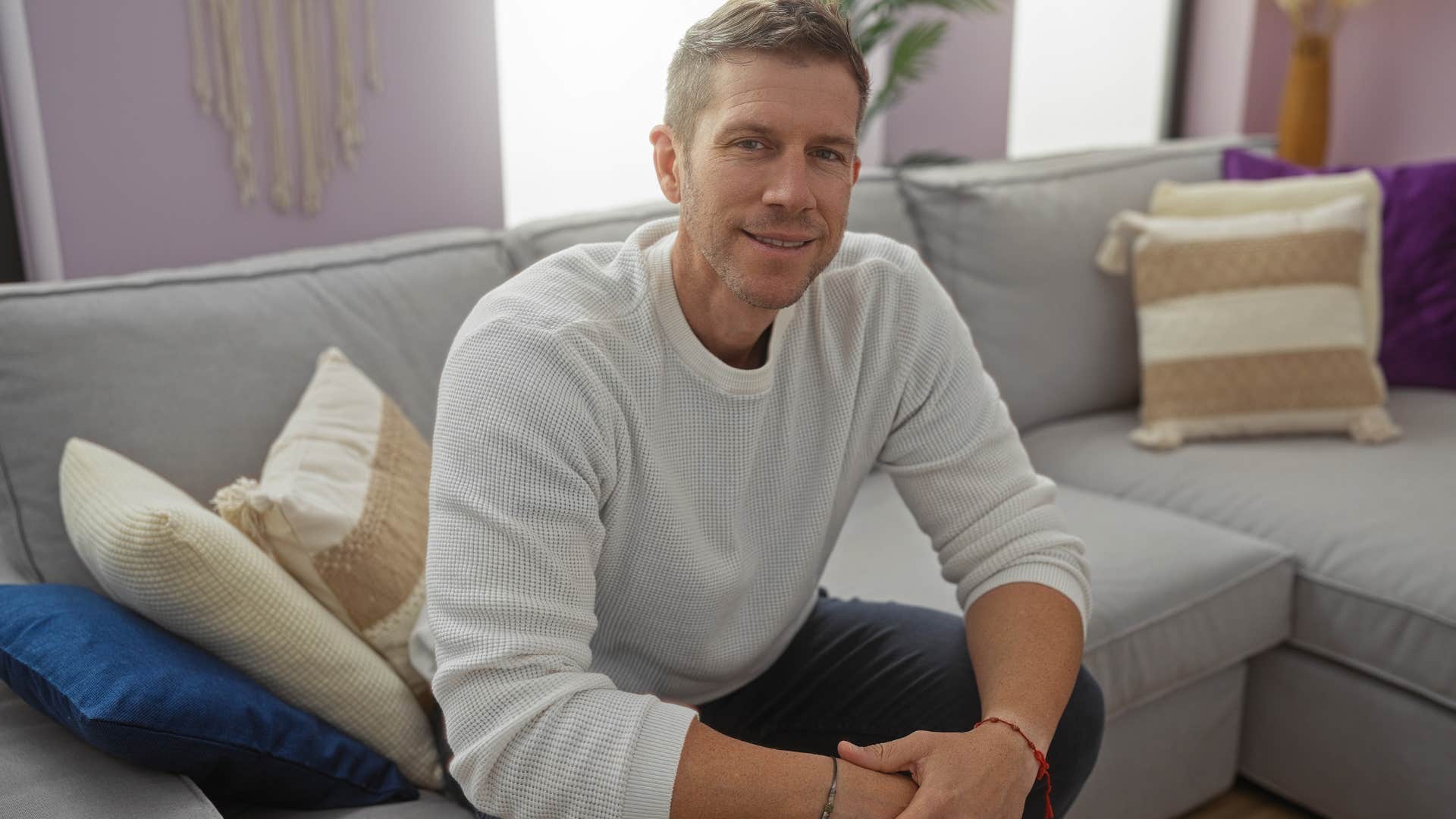man smiling on his couch with decorative pillows behind him