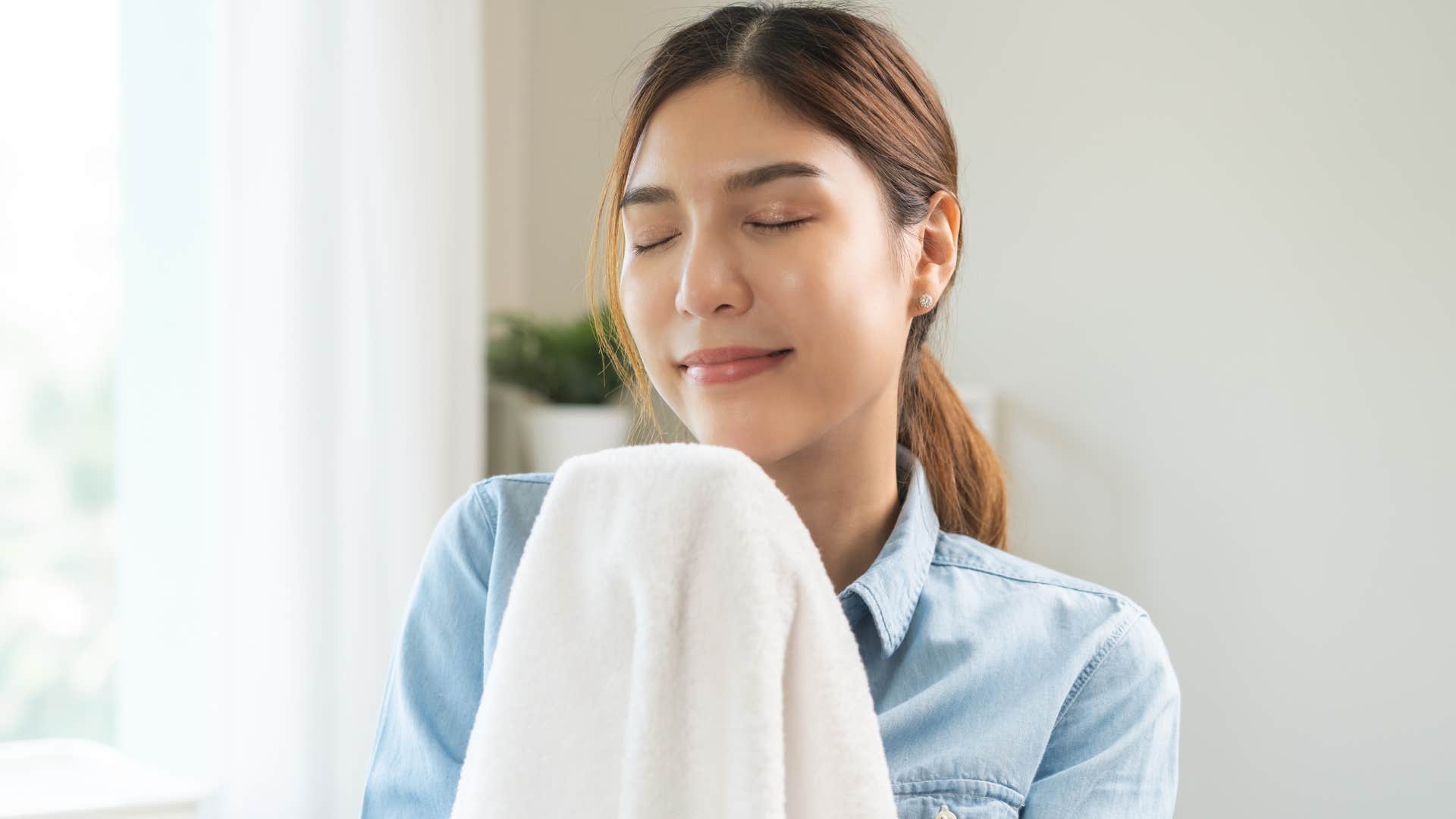 woman smiling and smelling towels at home
