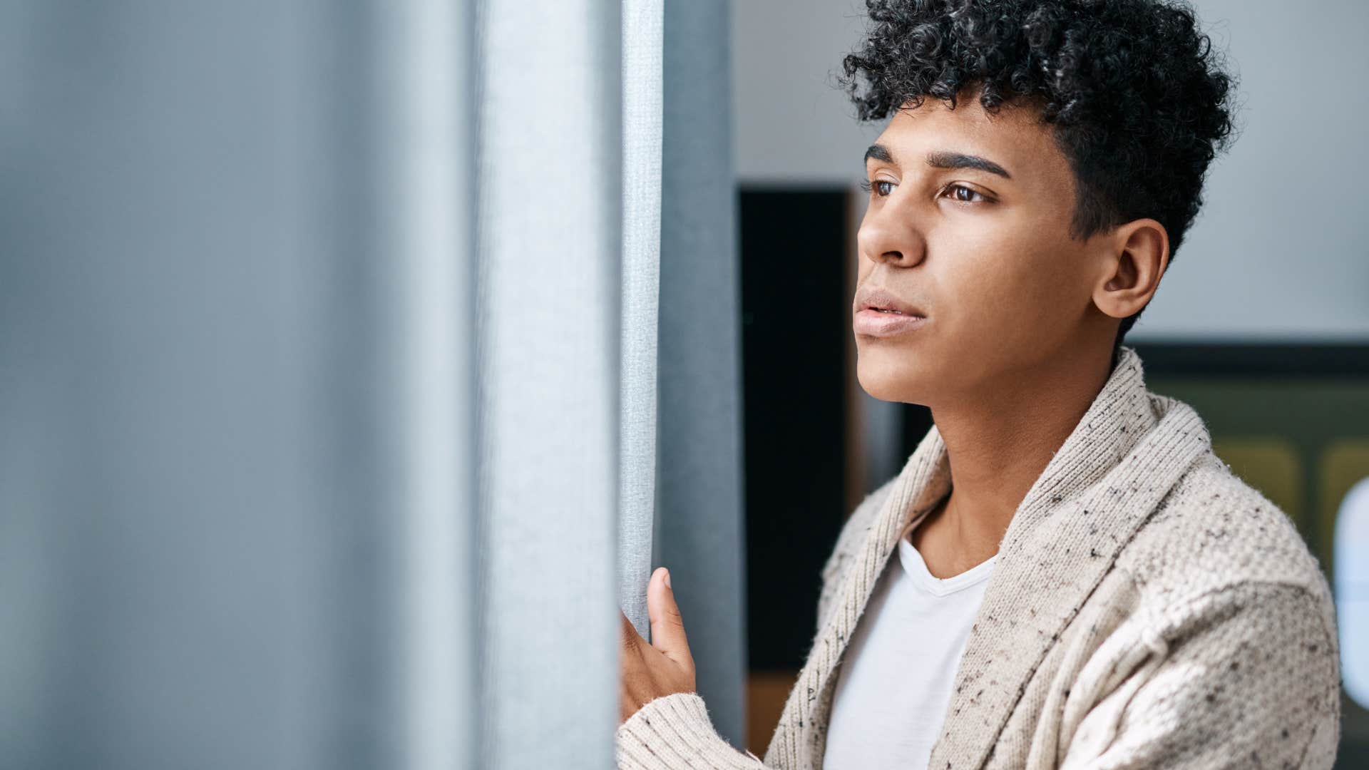 introverted man looking out window relieved he canceled plans