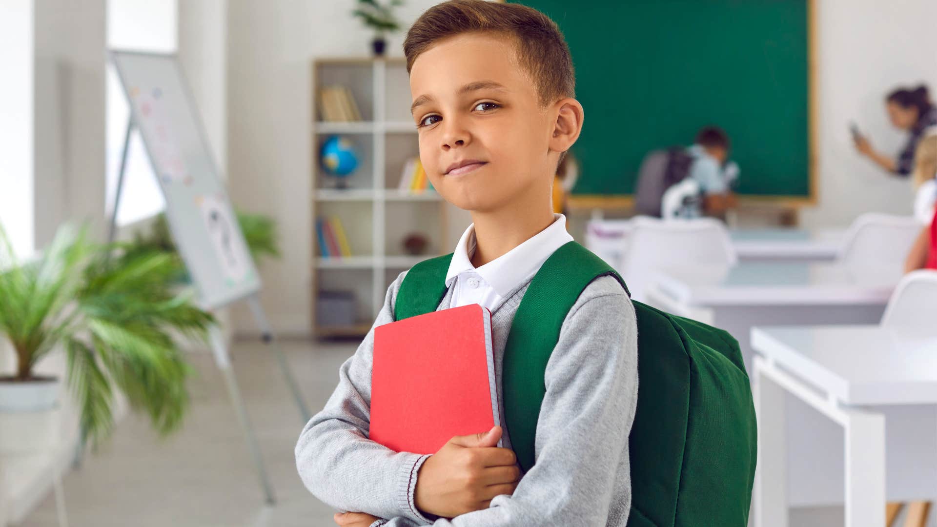 patient young boy smiling with his backpack on in a classroom