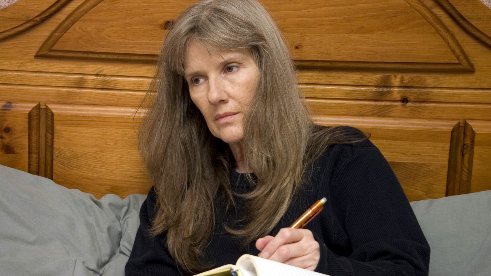 older woman who's dealt with hardship journaling in bed