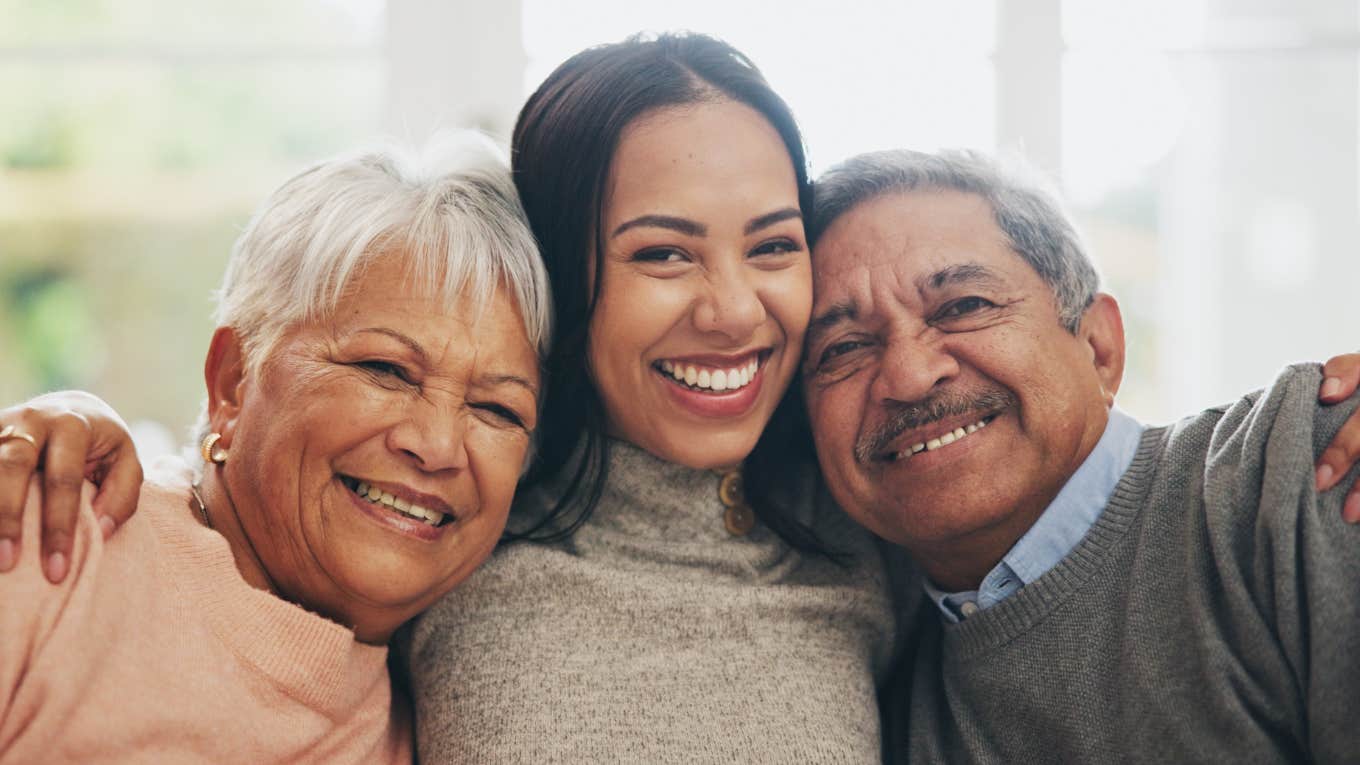 If These Things Still Feel Safe To You, You Were Truly Loved As A Kid adult woman in between her loving parents hugging and smiling