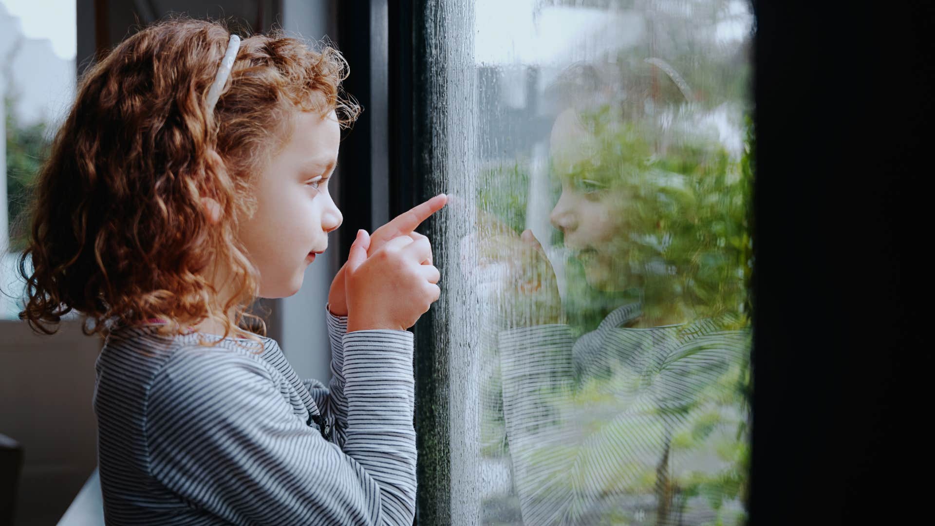 young girl looking out the window hearing the sound of rain