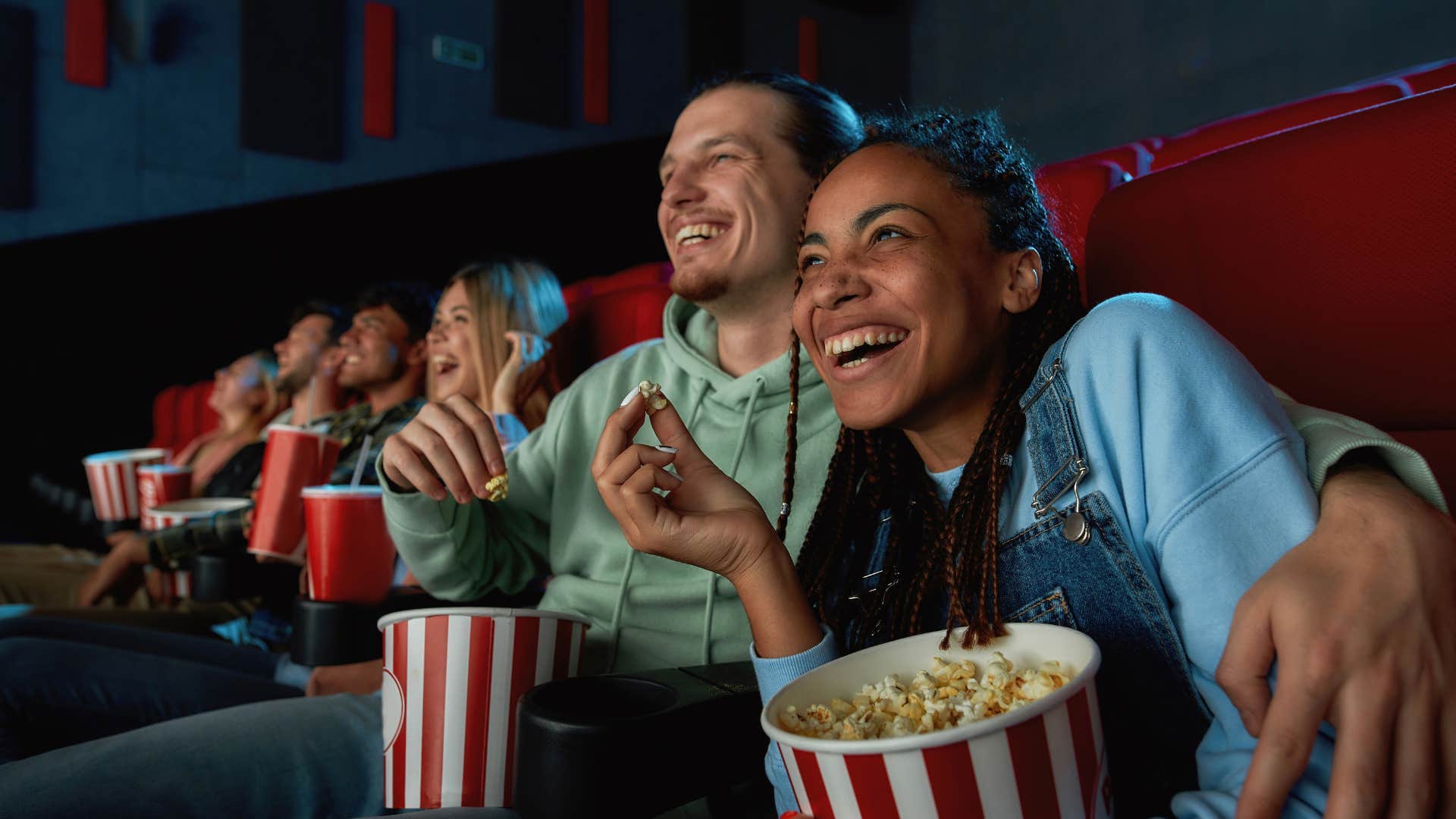 couple laughing at movie theater holding popcorn and snacks