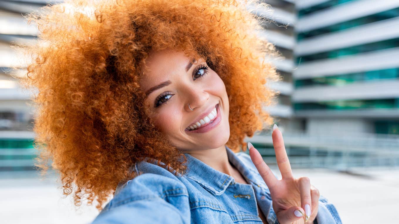 Brilliant Micro-Habits Of People Who Are 98% Happier Than Everyone Else woman smiling give peace sign looking happier than everyone else
