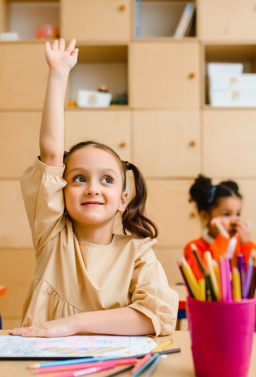 little girl raising her hand in school
