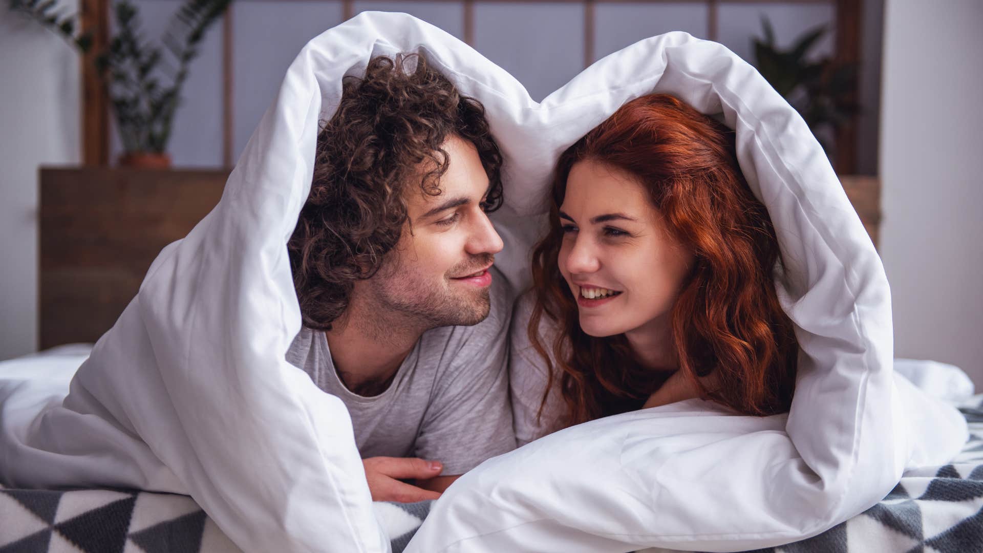 couple cuddling with one another under the blanket as they only have one blanket on the couch