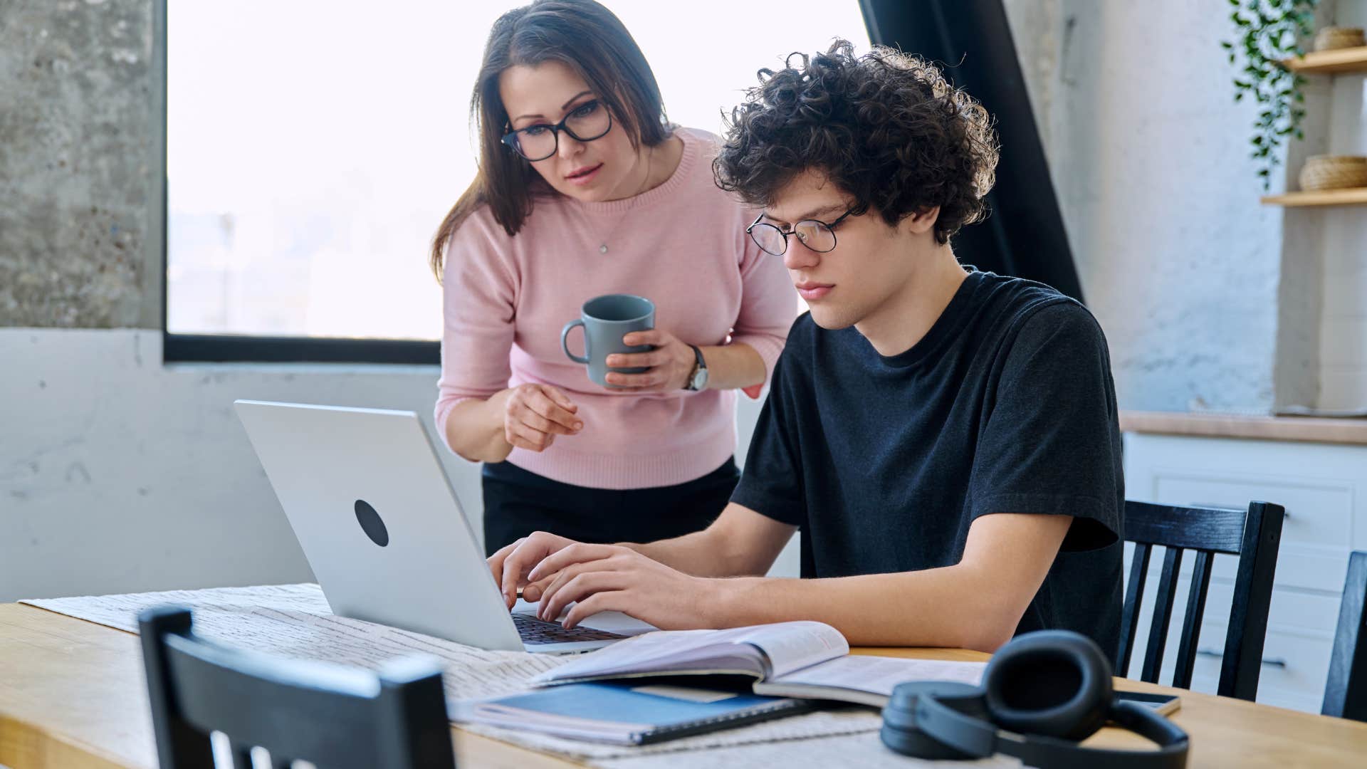 young boy sitting in front of laptop with mom looking over his shoulder