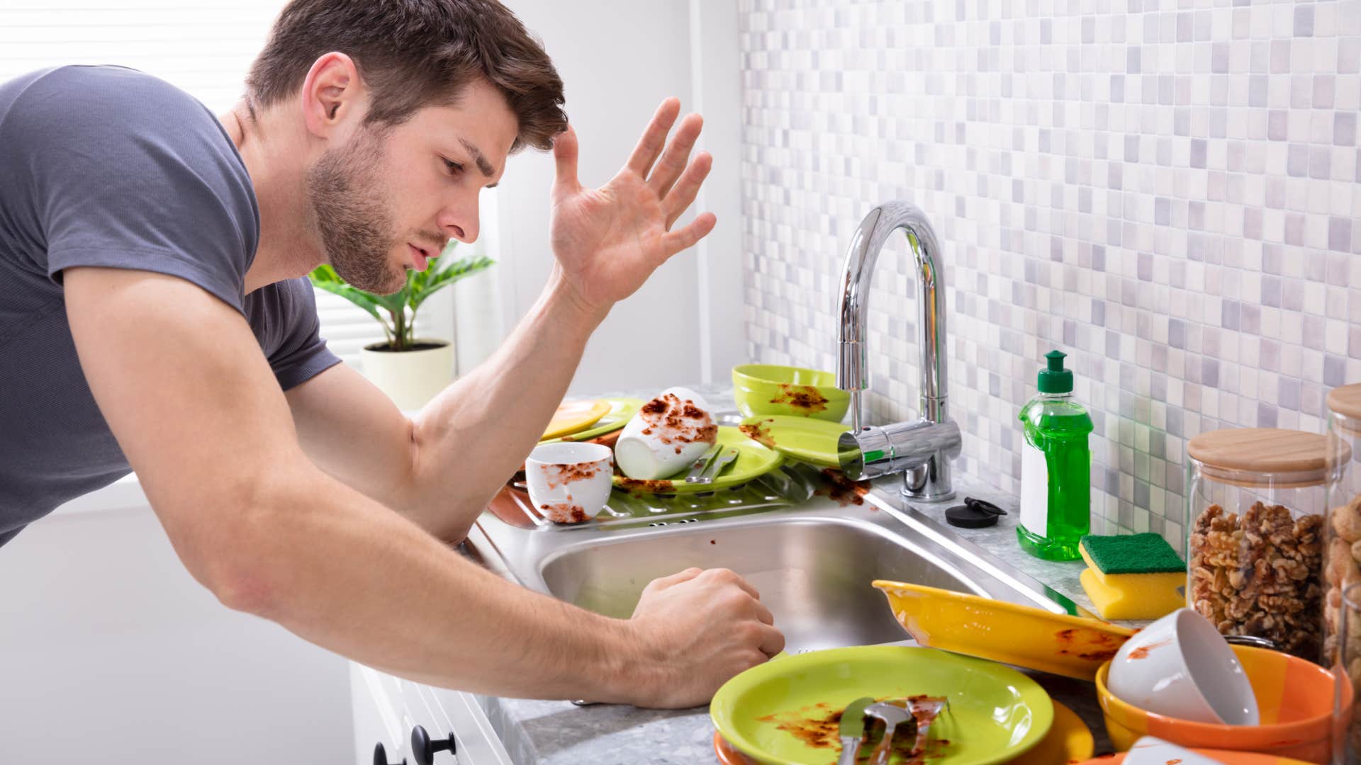sad man looking at overflowing dishes in sink