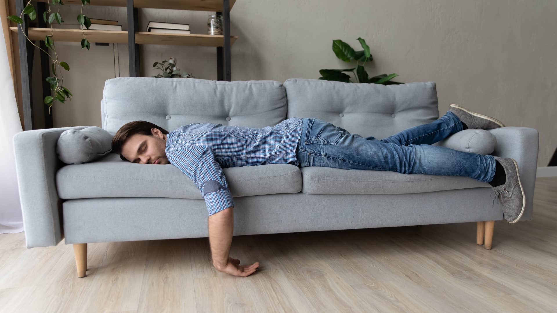 sad man sleeping in couch in front of empty walls and no decor
