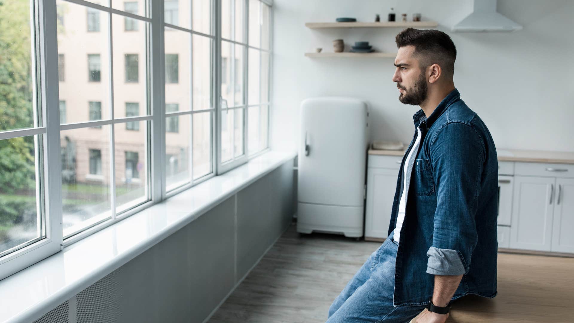 depressed man sitting in empty kitchen with no personal decor